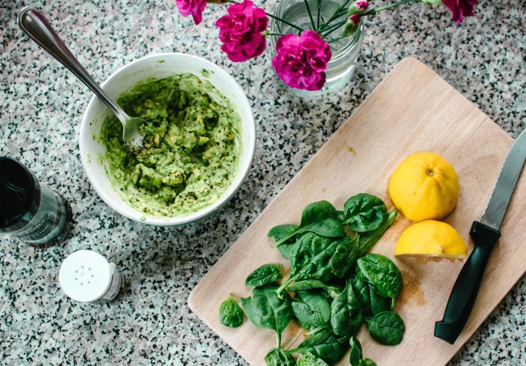 Guide to clean eating - A cut lemon with basil leaves, plus salt and pepper. Some ingredients mixed in a bowl with a fork. Fuchsia carnations in a glass.