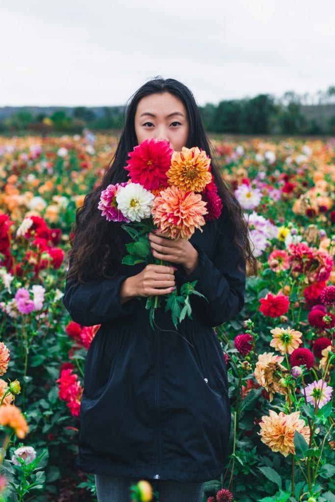 abundance mindset - a woman standing in a field of flowers holds a bright bouquet of flowers
