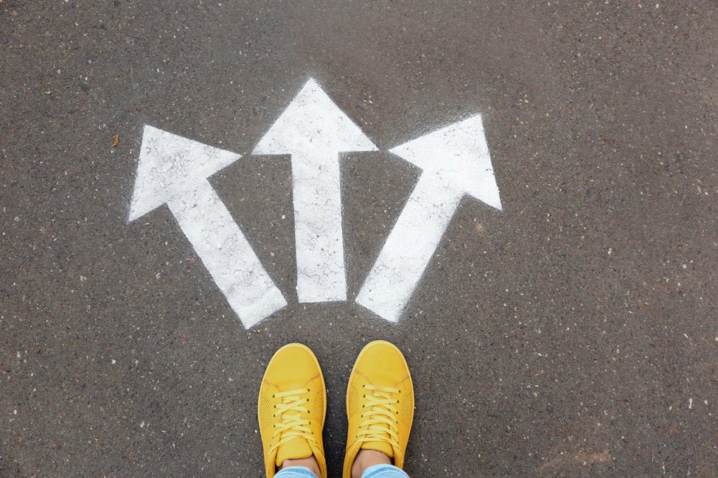 point of view shot of a person looking down at their feet with three arrows stenciled on pavement pointing in three separate directions