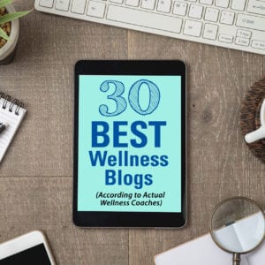 30 Best Wellness Blogs According to actual coaches square title graphic depicting a computer desk with keyboard, coffee, notepad and pen, and tablet computer.