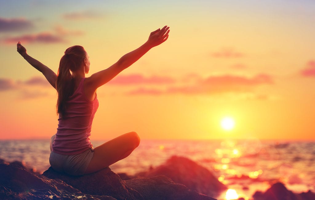 What is the Job Description of a Wellness Coach? 4 A wellness coaching student doing yoga by the ocean at sunset as she prepared to start her wellness journey.