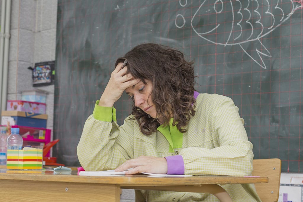 Teacher Burnout: Causes, Signs, and Help 2 A burned out teacher rubs her forehead while grading papers in an elementary school classroom.