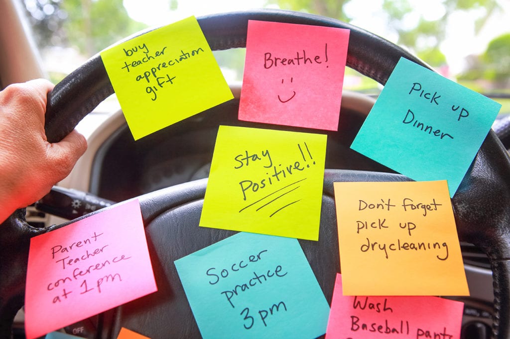 Car steering wheel covered in reminder sticky notes for a mother.