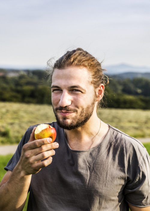 Young man eating an apple in rural landscape Young man eating an apple in rural landscape